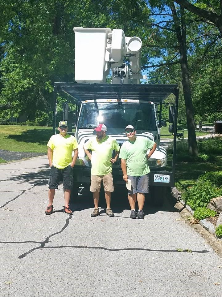 Three men are standing in front of a truck with a bucket on top of it.