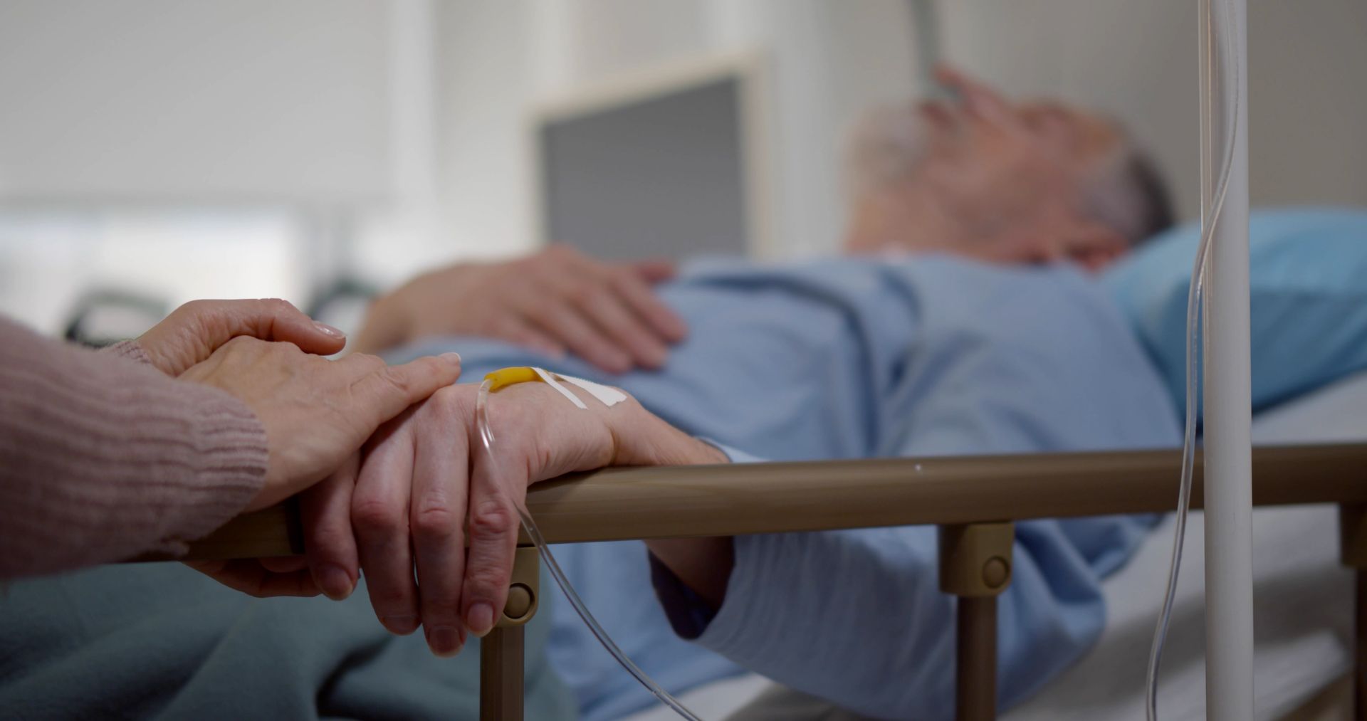 Hospital room with an empty bed, wheelchair, and teal lighting near a window.