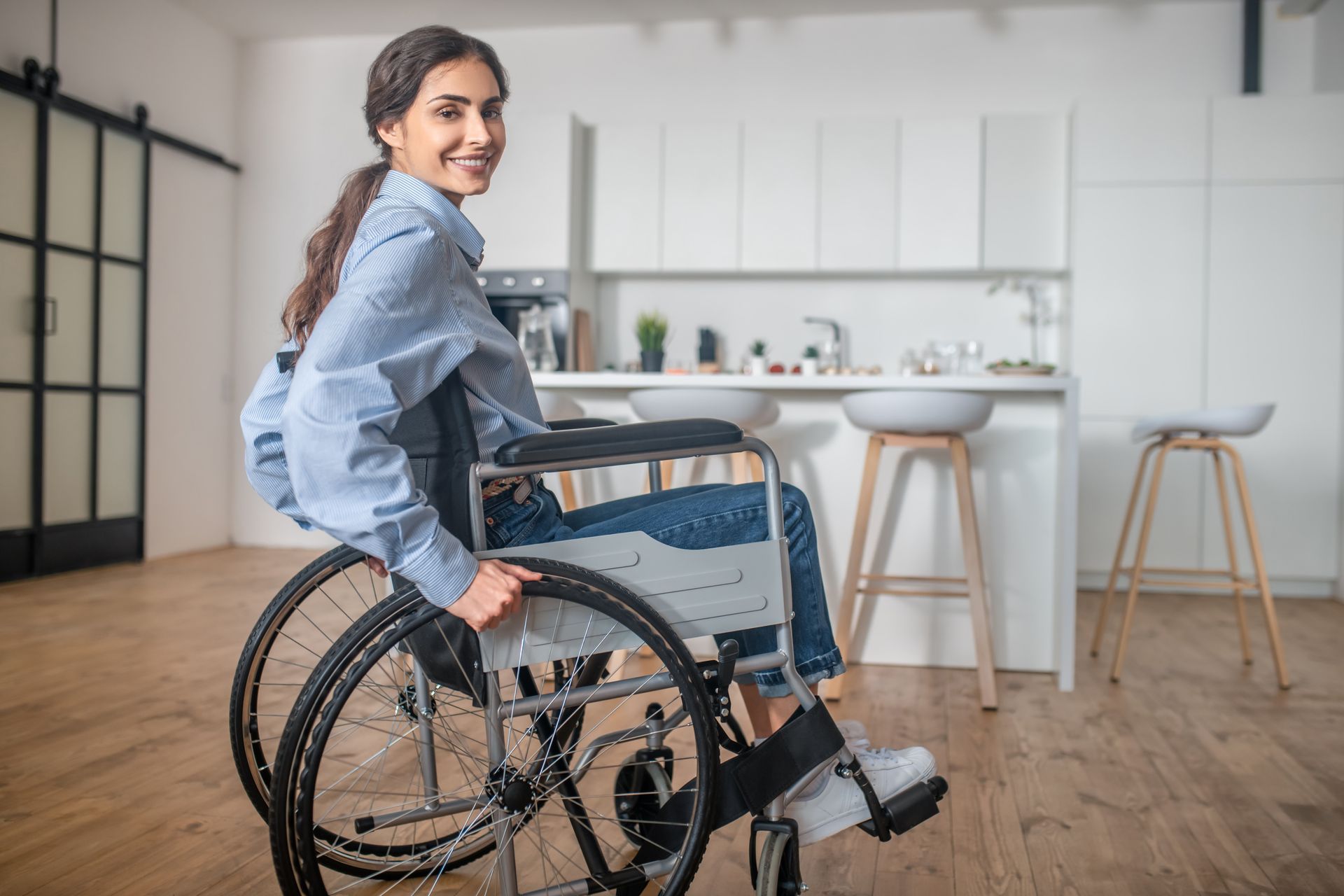 Person in a wheelchair smiling in a bright kitchen beside a counter and stools