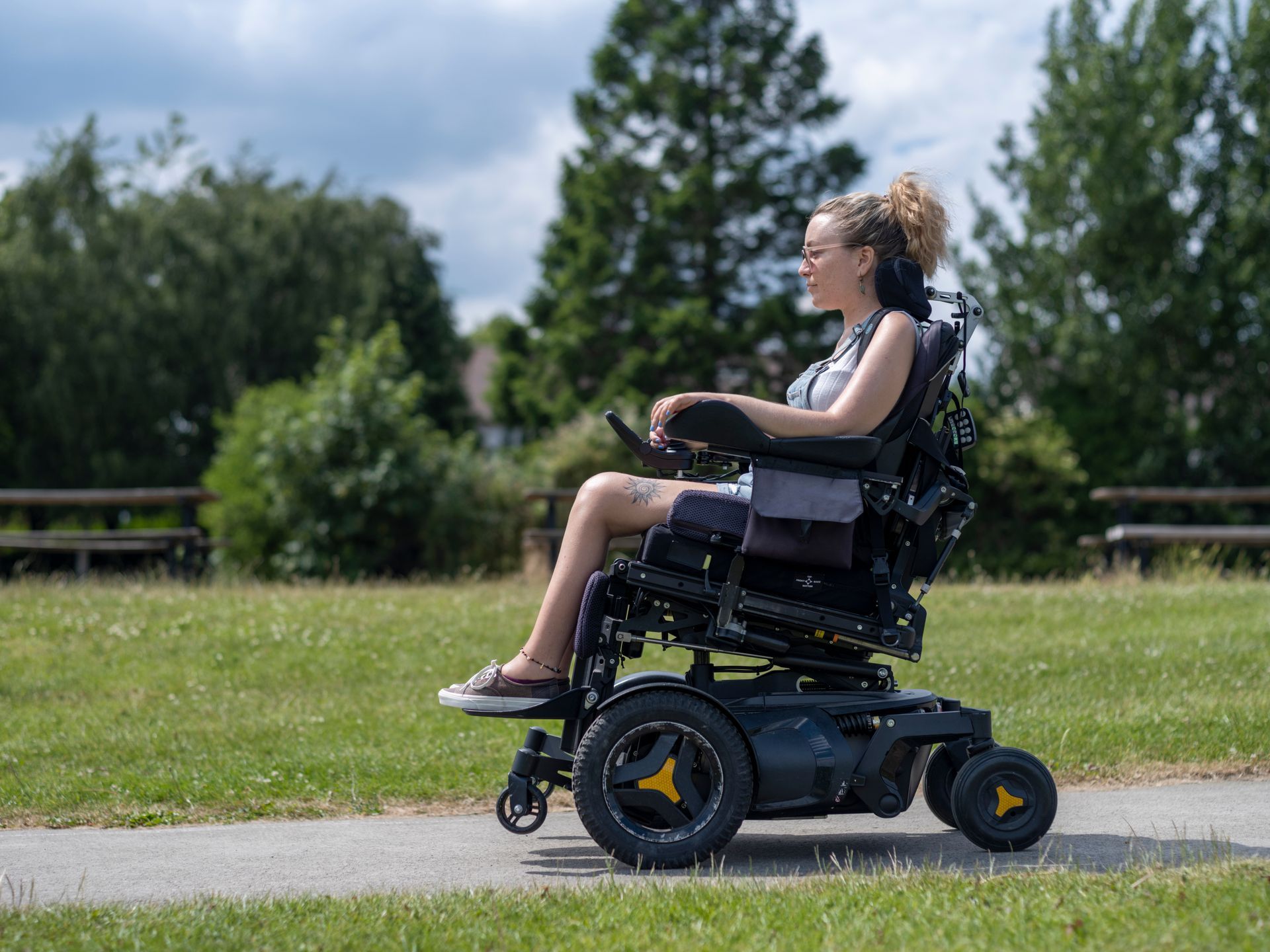 Person in a motorized wheelchair riding on a paved path in a grassy park.