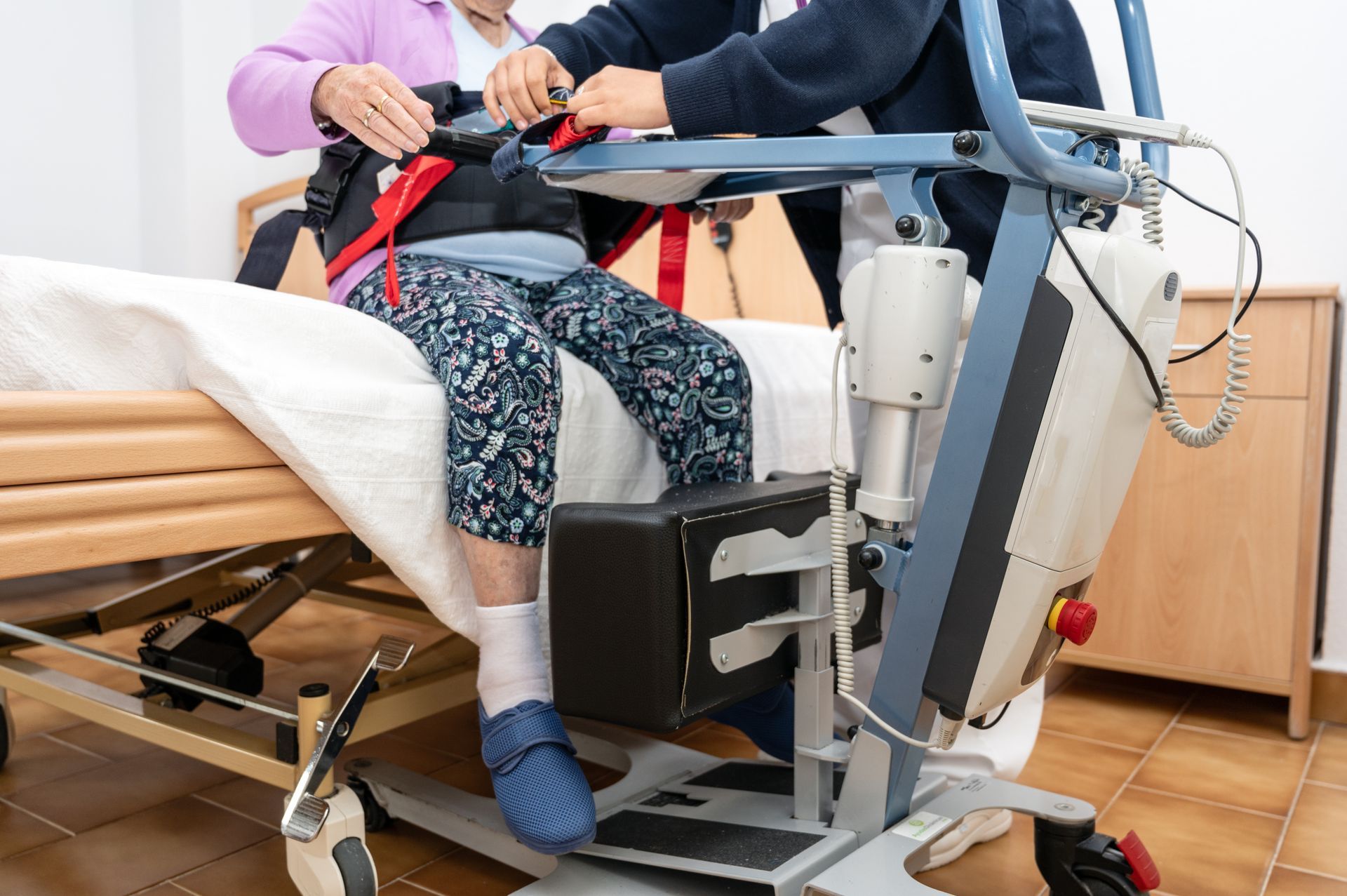 Caregiver assists a person in a hospital bed using a standing transfer aid