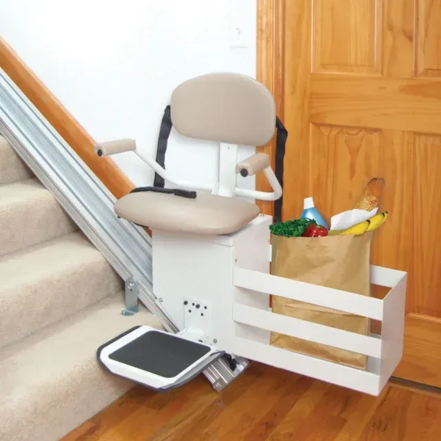 Stairlift chair on a wooden stairway beside a grocery bag and white rail