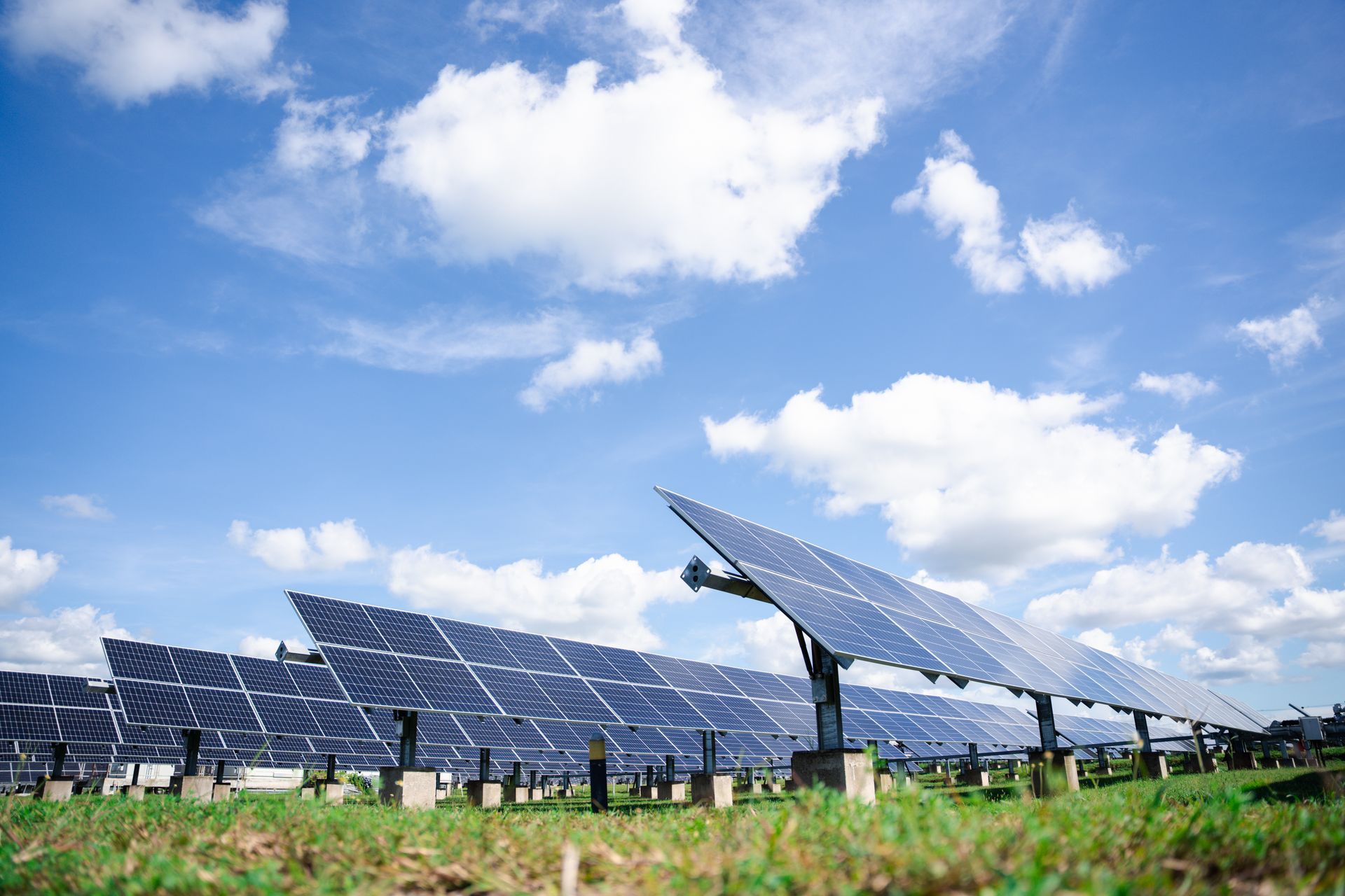 Solar panels in a field against a bright blue sky with fluffy white clouds. Solar panels in a field against a bright blue sky with fluffy white clouds.