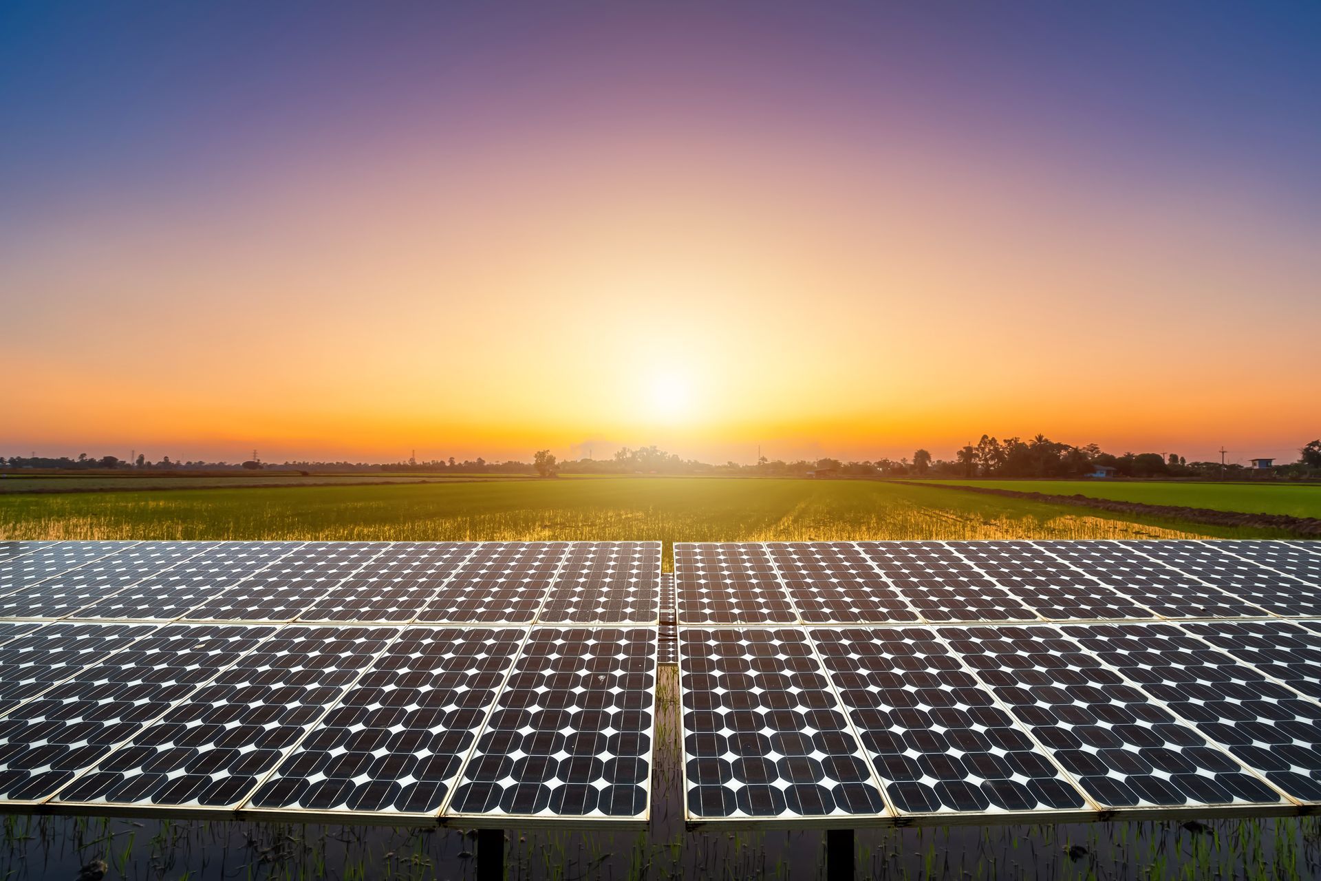 Solar panels in a field at sunset with a vibrant orange and blue sky. Solar panels in a field at sunset with a vibrant orange and blue sky.