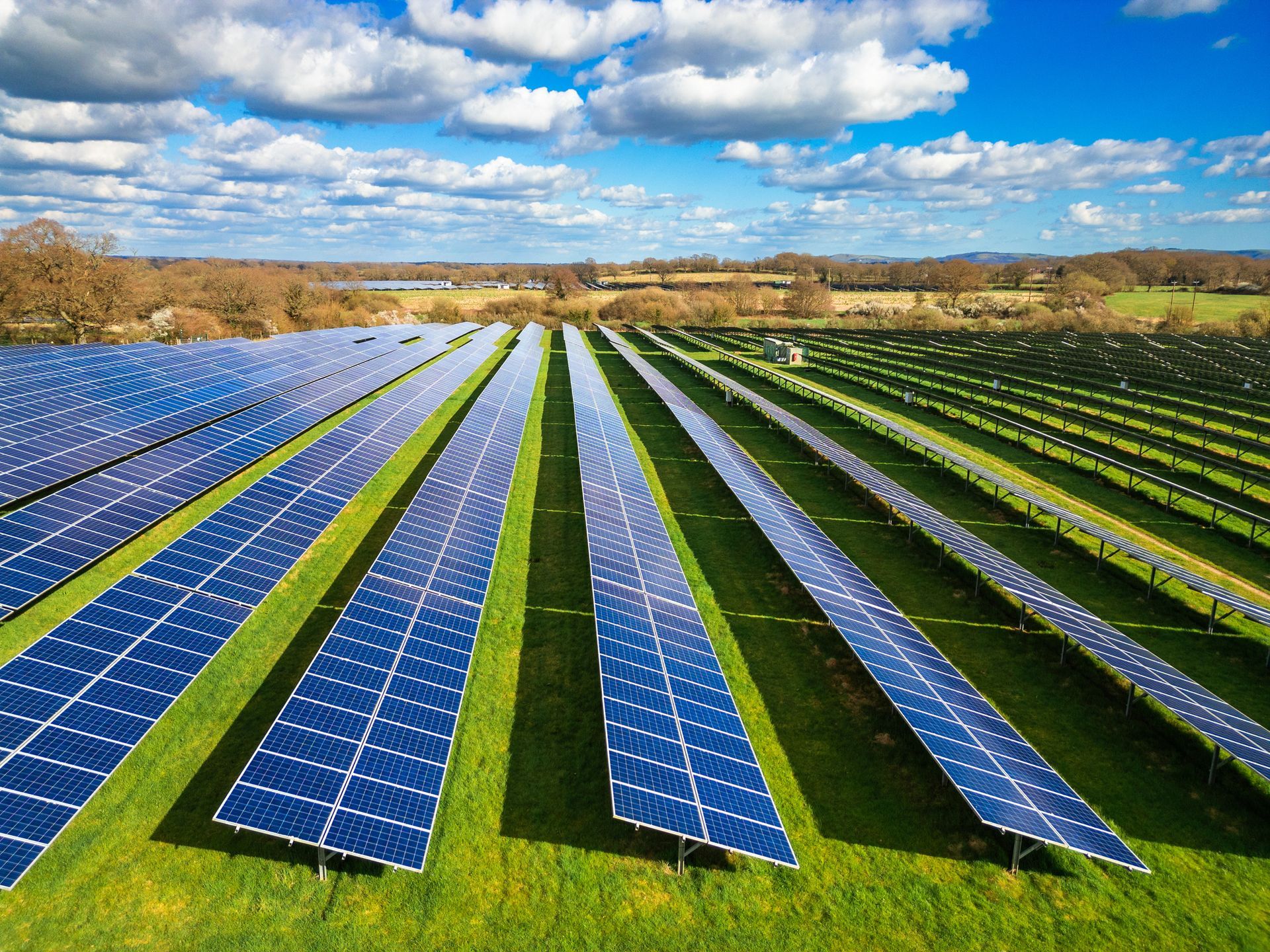 Solar panels arranged in rows on a grassy field under a blue sky with clouds. Solar panels arranged in rows on a grassy field under a blue sky with clouds.