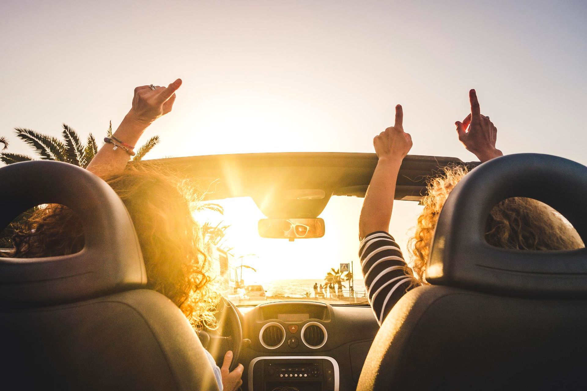 Two women are sitting in a car with their arms in the air.