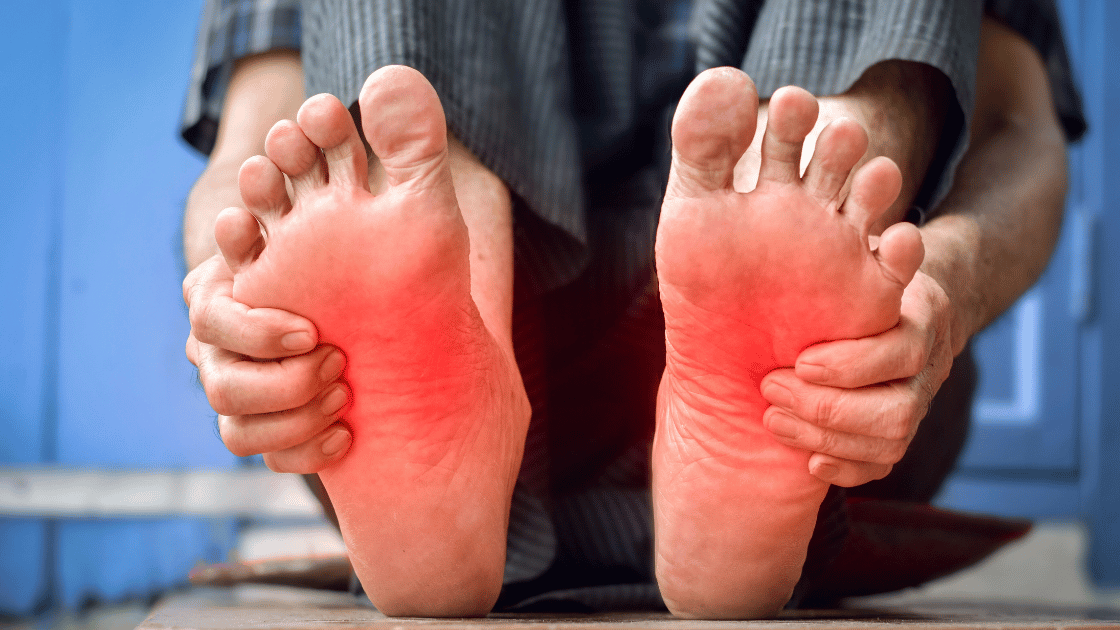 Person sitting with bare feet held up, soles visibly red against a blue background