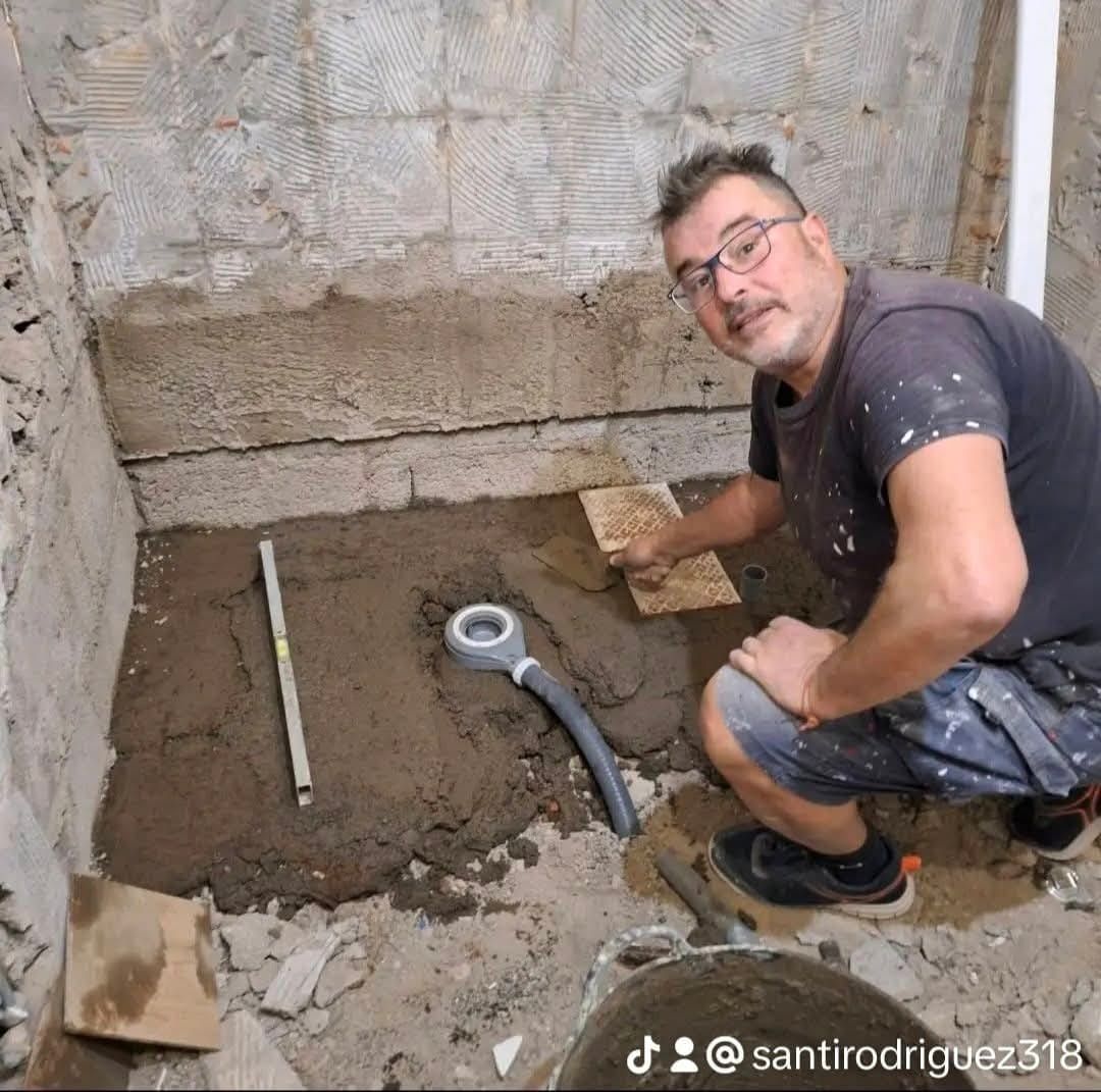 Un hombre está arrodillado en una habitación con una manguera y una regla.