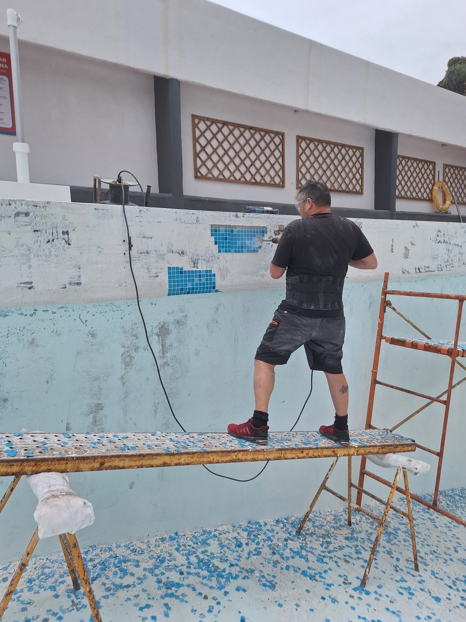 Un hombre está de pie sobre un andamio sobre una piscina.