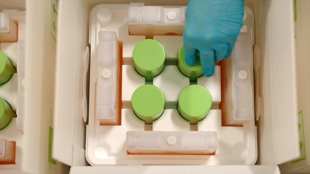 Gloved hand handling containers of radioactive drug.