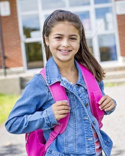 Smiling student with pink backpack standing outside a school building