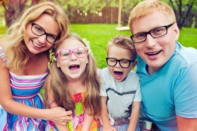 Smiling family of four with colorful glasses posing outdoors in a green park
