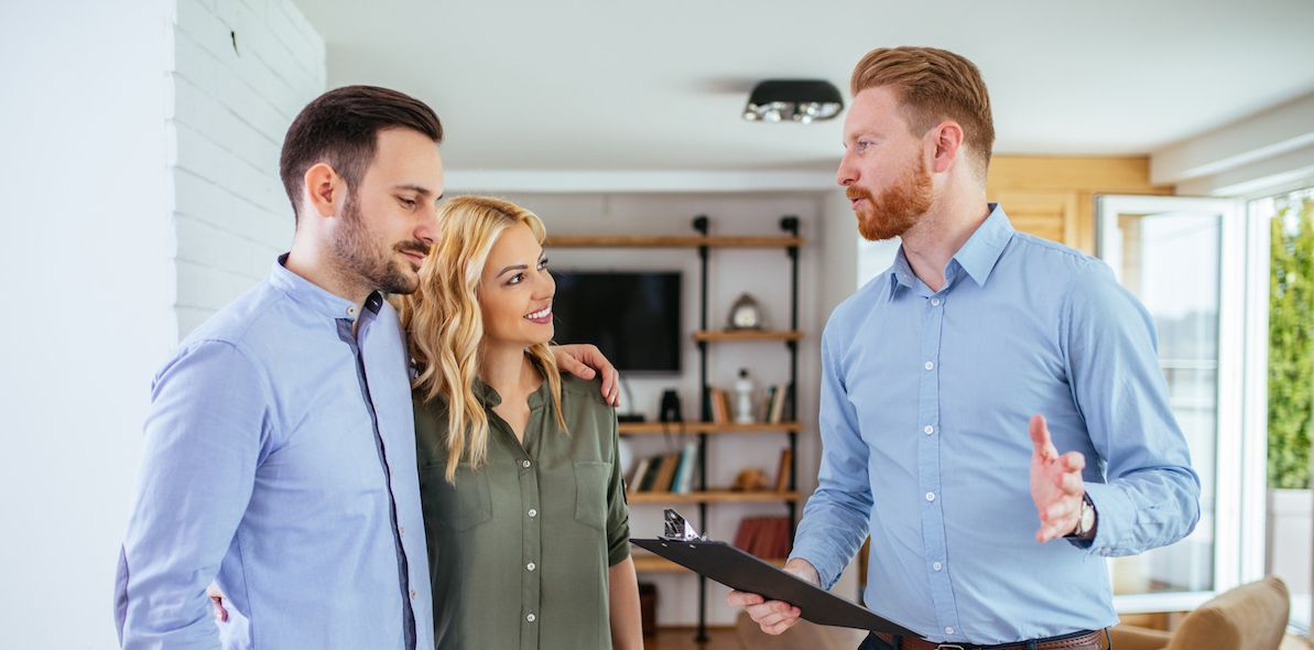 A man is holding a clipboard and talking to a couple in a living room.