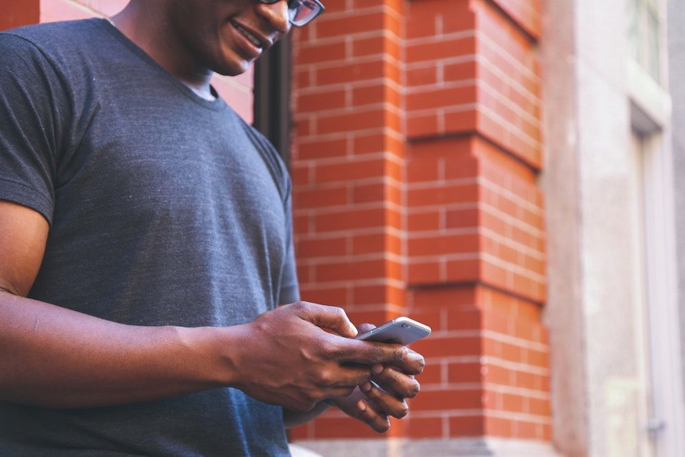 A man is standing in front of a brick building looking at his cell phone.