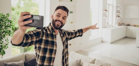 A man is taking a selfie with his cell phone in a living room.
