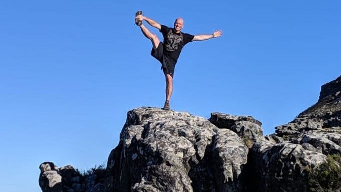 A man is standing on one leg on top of a rock.