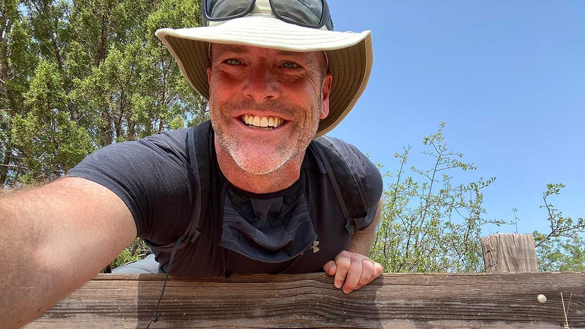A man wearing a hat and sunglasses is taking a selfie.