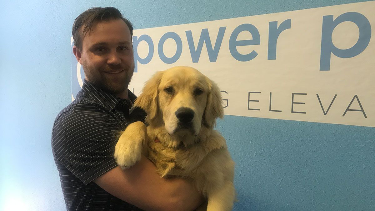 A man is holding a puppy in front of a sign that says power