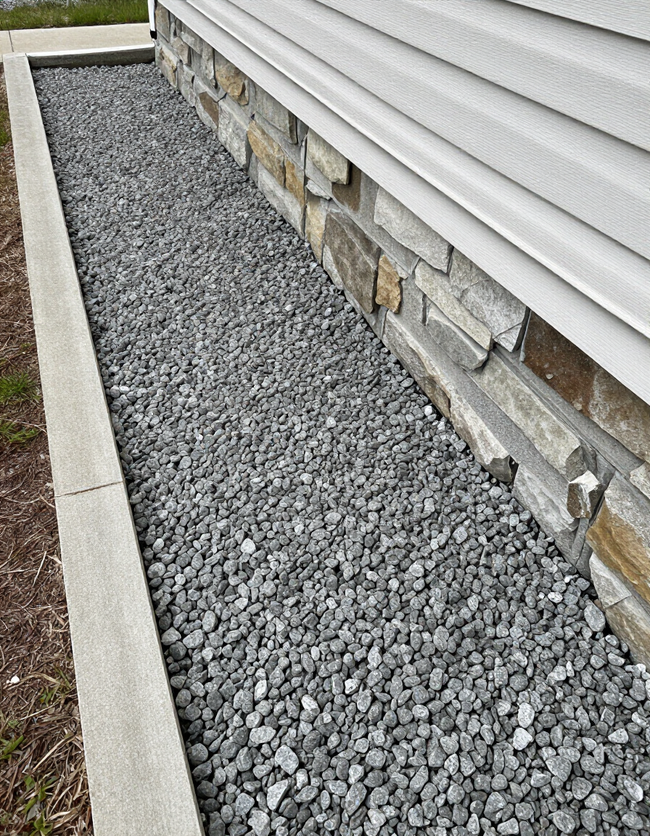 Gray gravel strip along a house foundation beside white siding and stone veneer