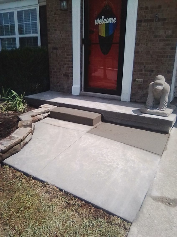 Front porch entrance with a concrete accessibility ramp leading to a red welcome door, flanked by brick steps.