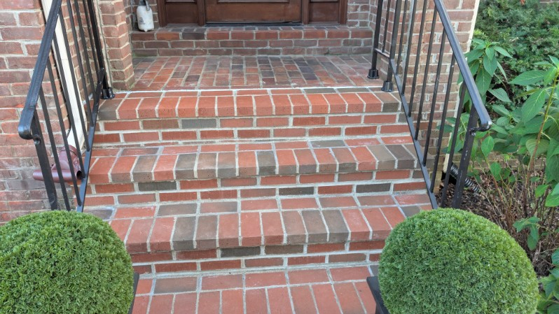 Brick front steps with black railings and trimmed shrubs leading to a house entry