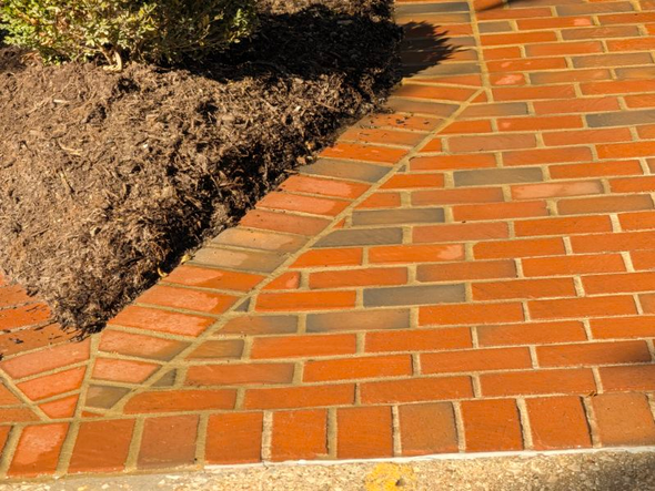 Brick walkway beside a landscaped bed with soil and mulch