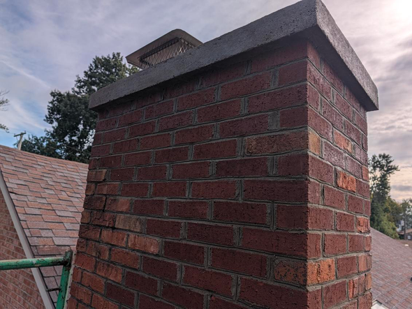 Red brick chimney with a gray concrete cap against a cloudy sky