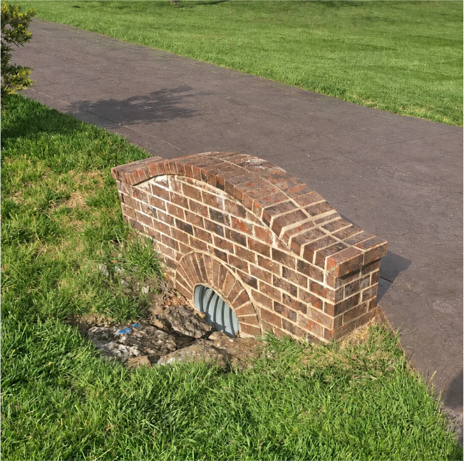 Brick storm drain culvert beside a paved path and grassy lawn