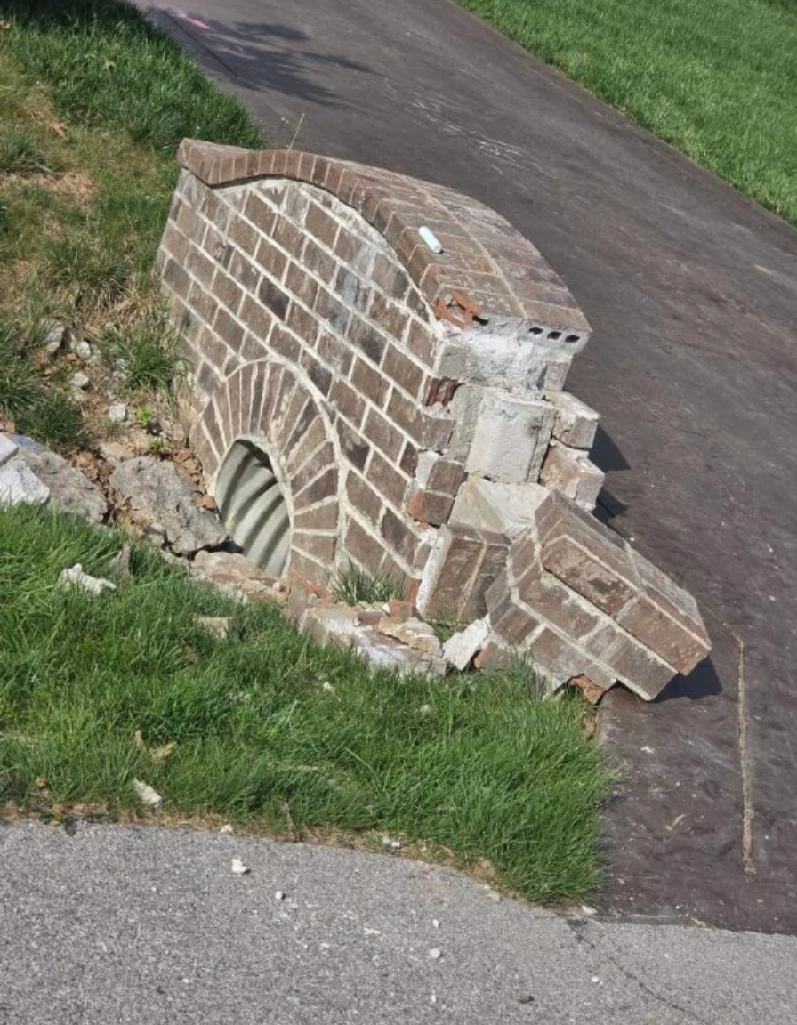 Broken brick culvert beside a driveway, with a collapsed arch and scattered rubble.