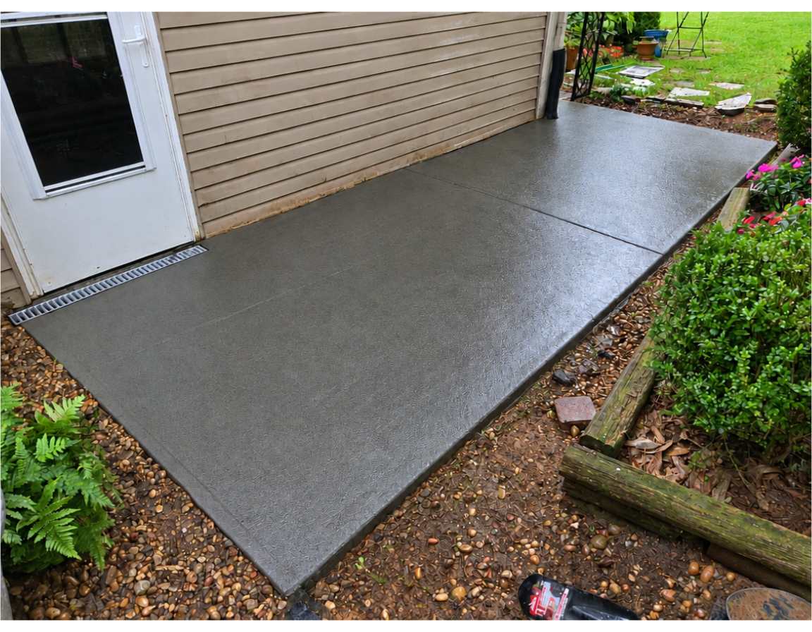 Freshly poured concrete patio beside a house, bordered by mulch and garden plants