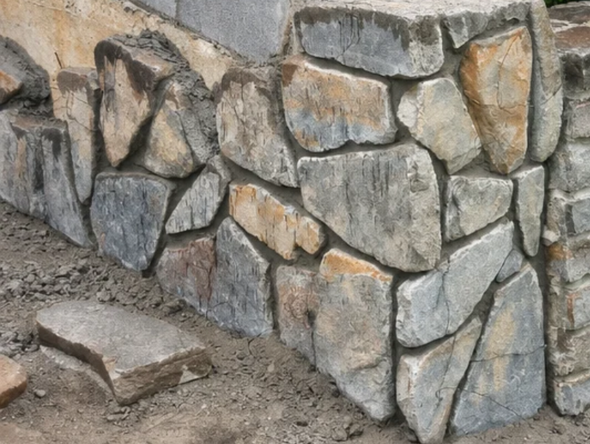 Stone retaining wall with irregular gray and tan rocks beside a dirt path