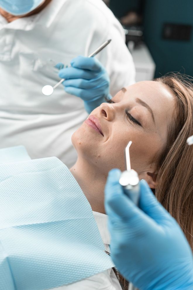 Una donna è seduta sulla poltrona del dentista mentre un dentista le visita i denti.