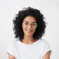 A woman with curly hair and glasses is wearing a white shirt.