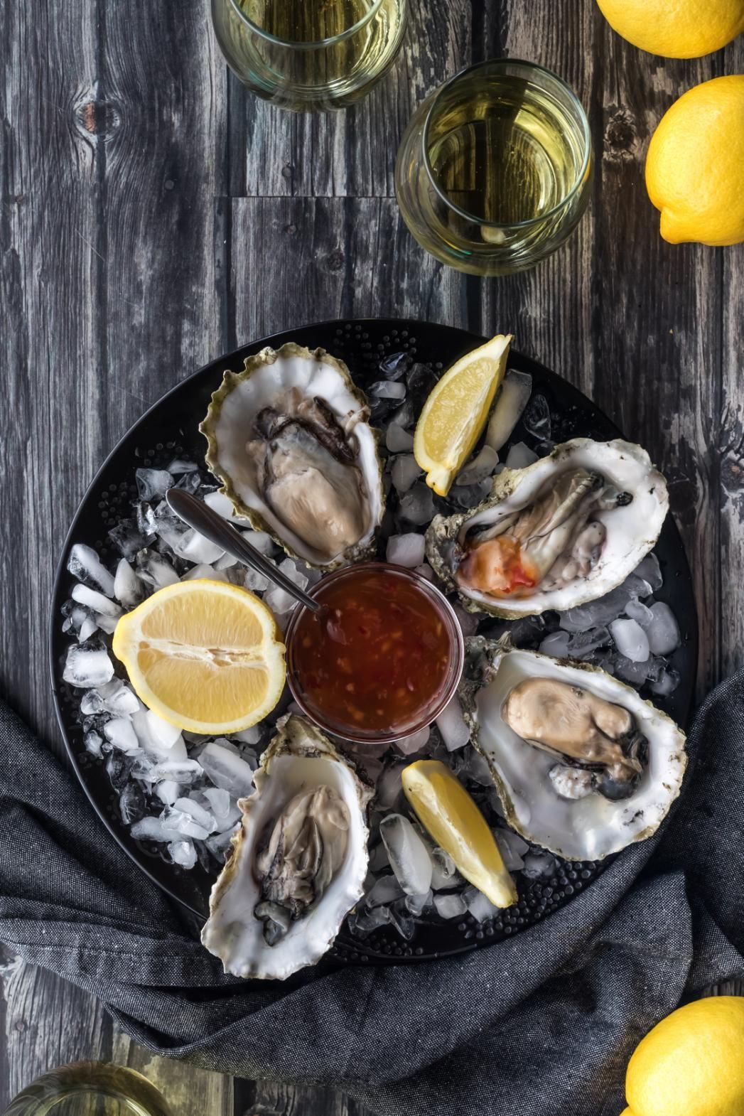 Oysters on ice with lemon wedges and dipping sauce on a dark rustic table