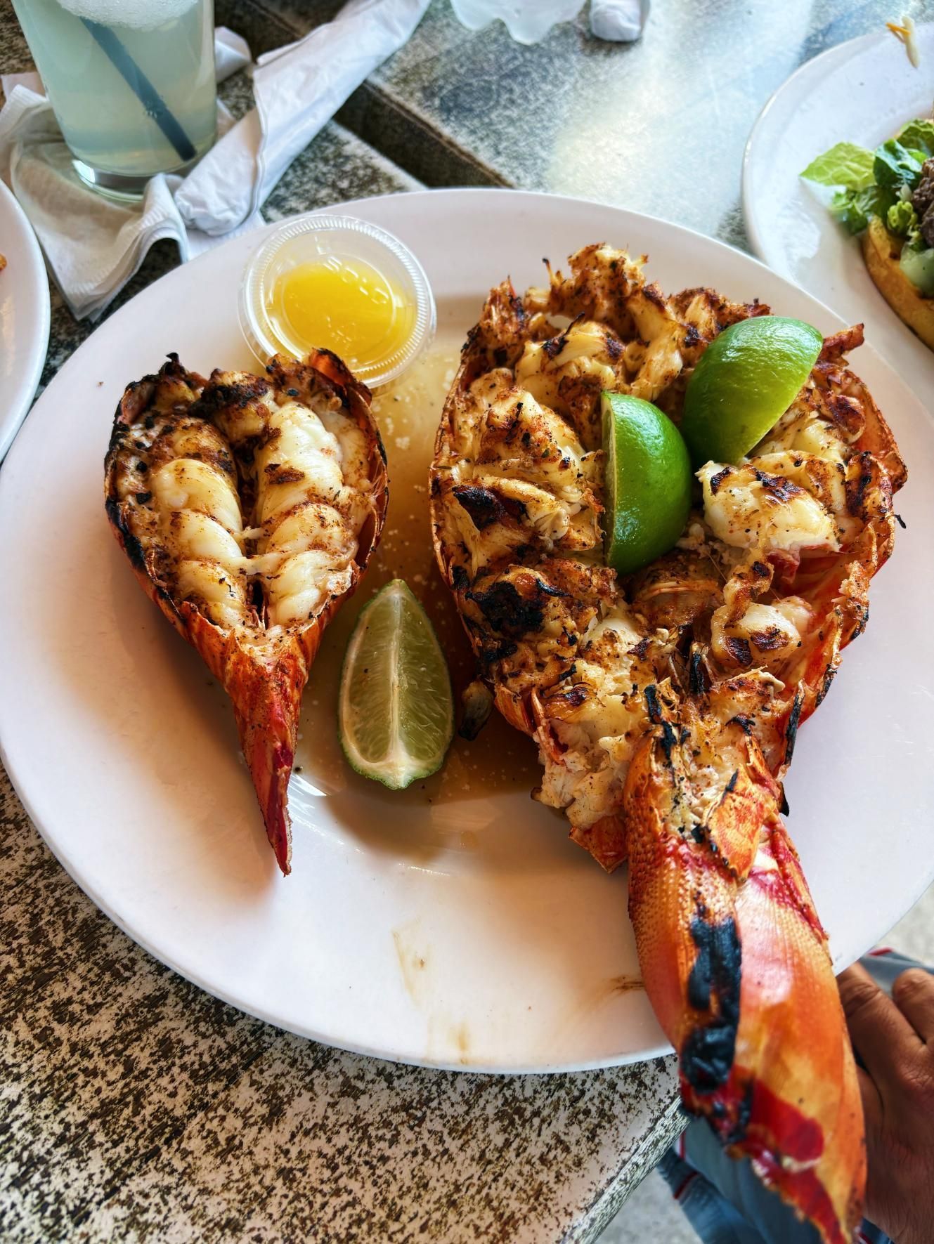 Plated grilled lobster tails with lemon and lime wedges on a white dish.