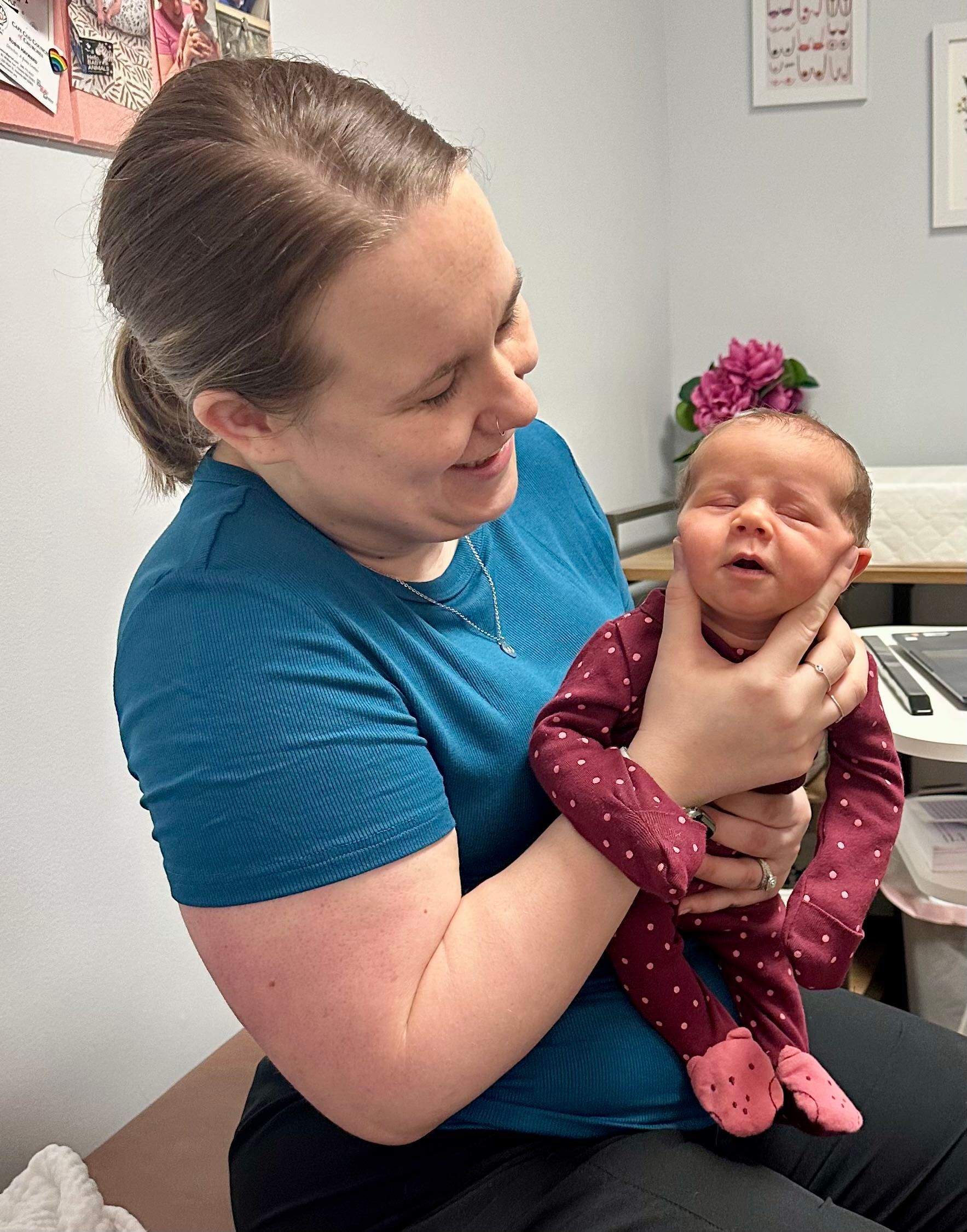 Woman holding newborn baby, both looking at each other, in a room with a flower.