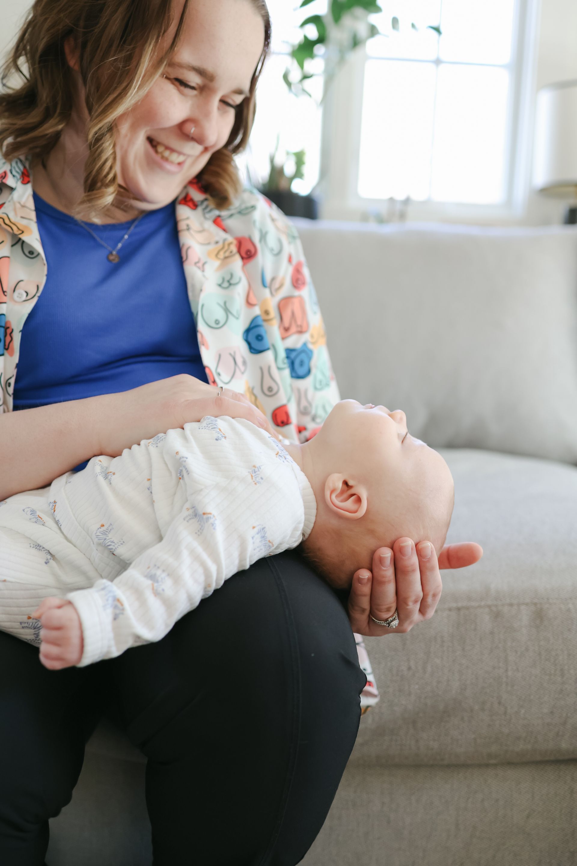 Woman holding and looking at baby on her lap; smiling indoors.
