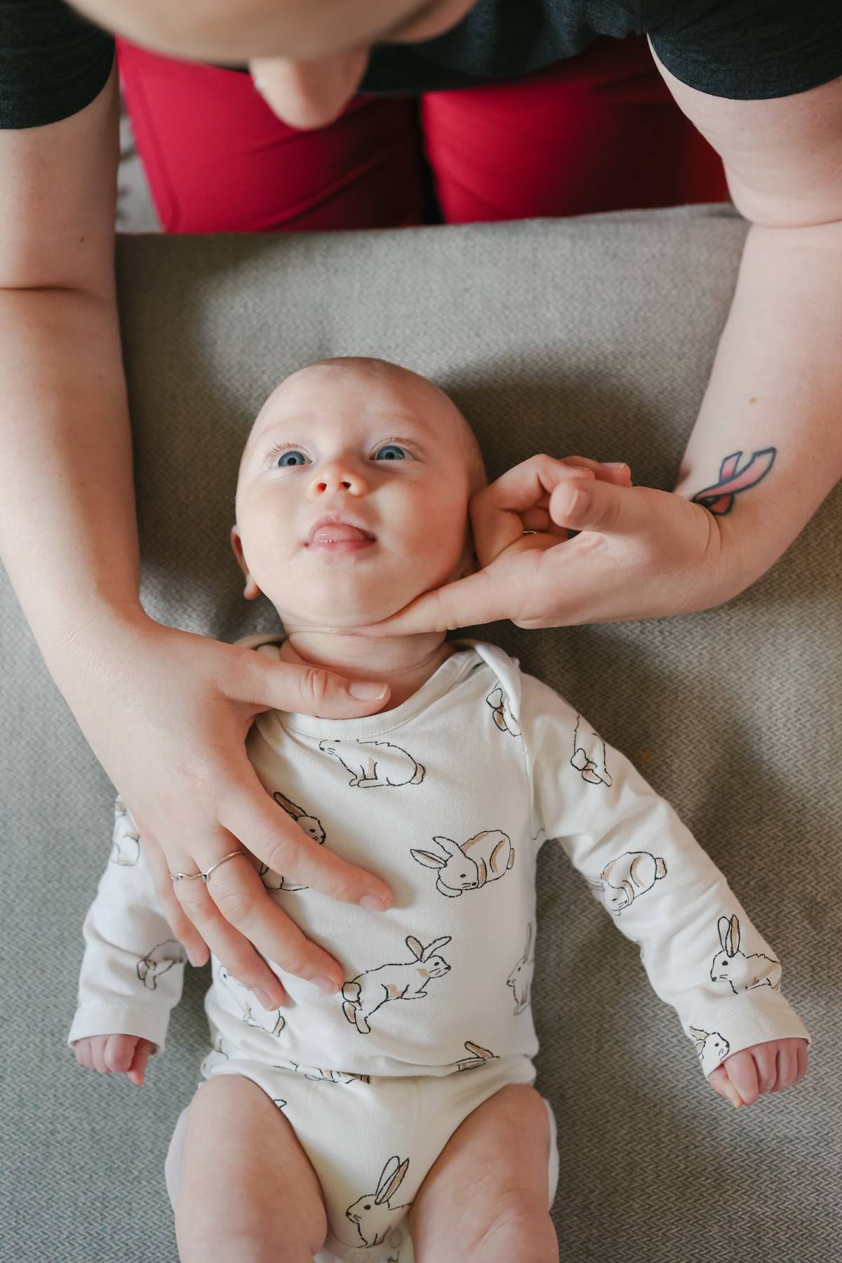 Person gently examining the neck of a baby in a bunny-patterned onesie.