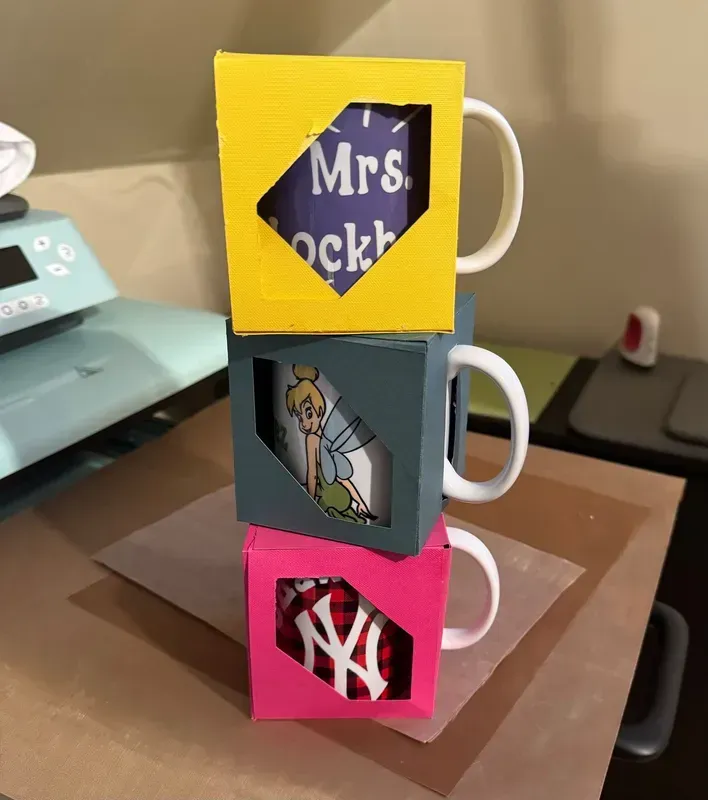 Three mugs stacked, each with a colored box frame and a design peeking through a cut-out.