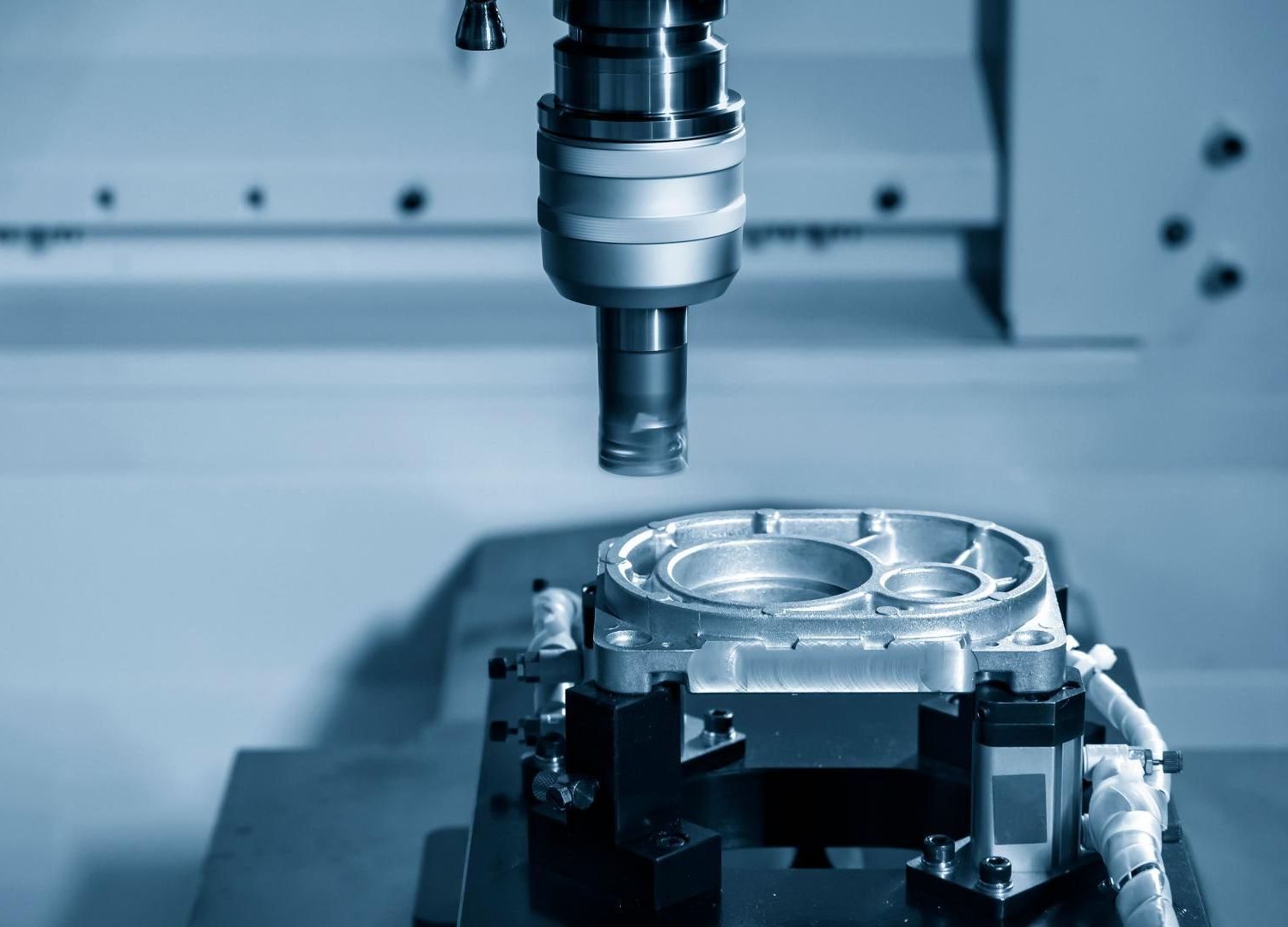 Machine CNC en train de découper une pièce métallique sous une broche dans un atelier éclairé en bleu