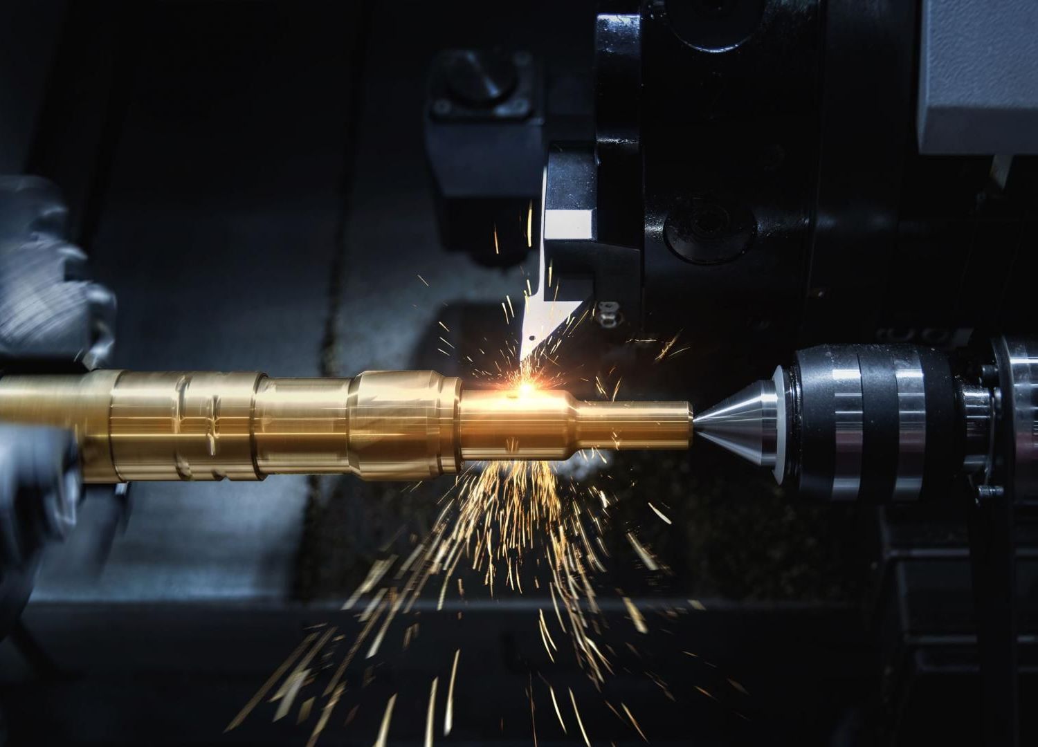 Une tige métallique est découpée avec précision sur un tour, des étincelles jaillissant dans un atelier sombre.
