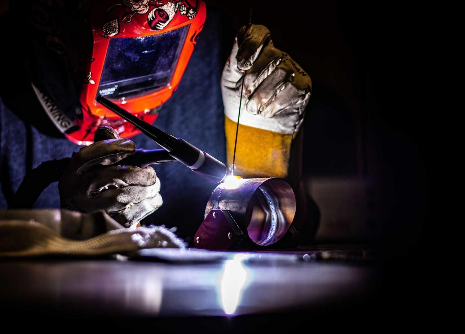 Soudeur en casque rouge travaillant du métal, arc lumineux éclairant une scène d'atelier sombre