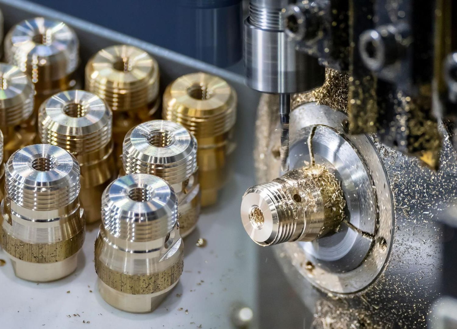 Des pièces métalliques sont usinées sur un tour à commande numérique, avec des composants en or et en argent dans un atelier.