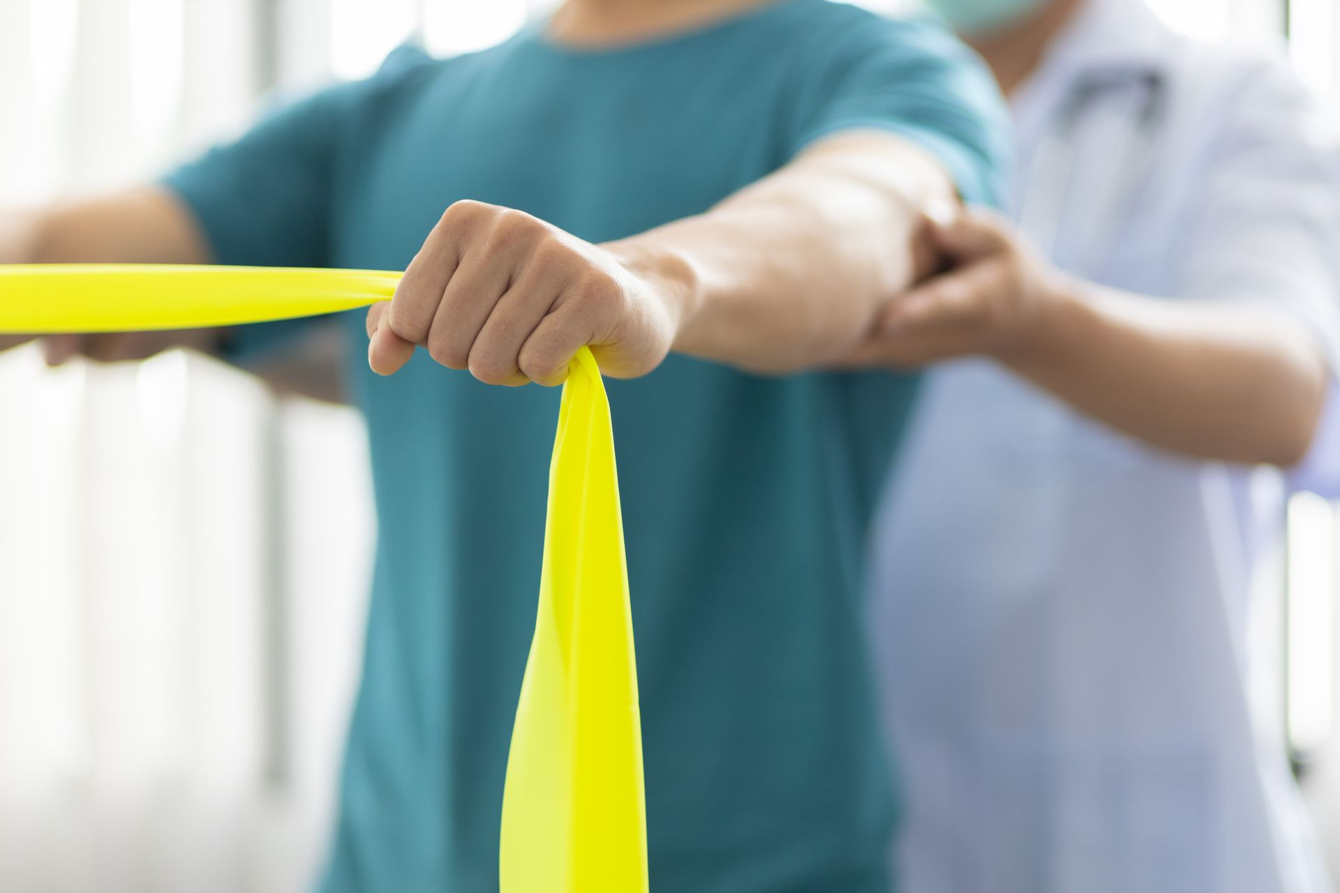 Persona che utilizza una fascia elastica gialla per fare esercizio, assistita da un fisioterapista.