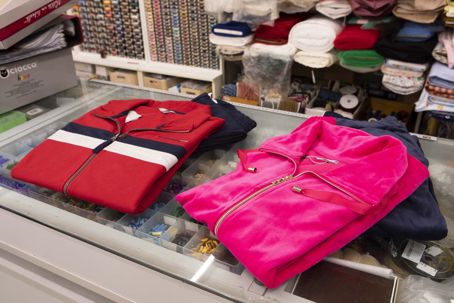 Giacche con cerniera rosse e rosa su una superficie di vetro, con materiali per cucire sullo sfondo.