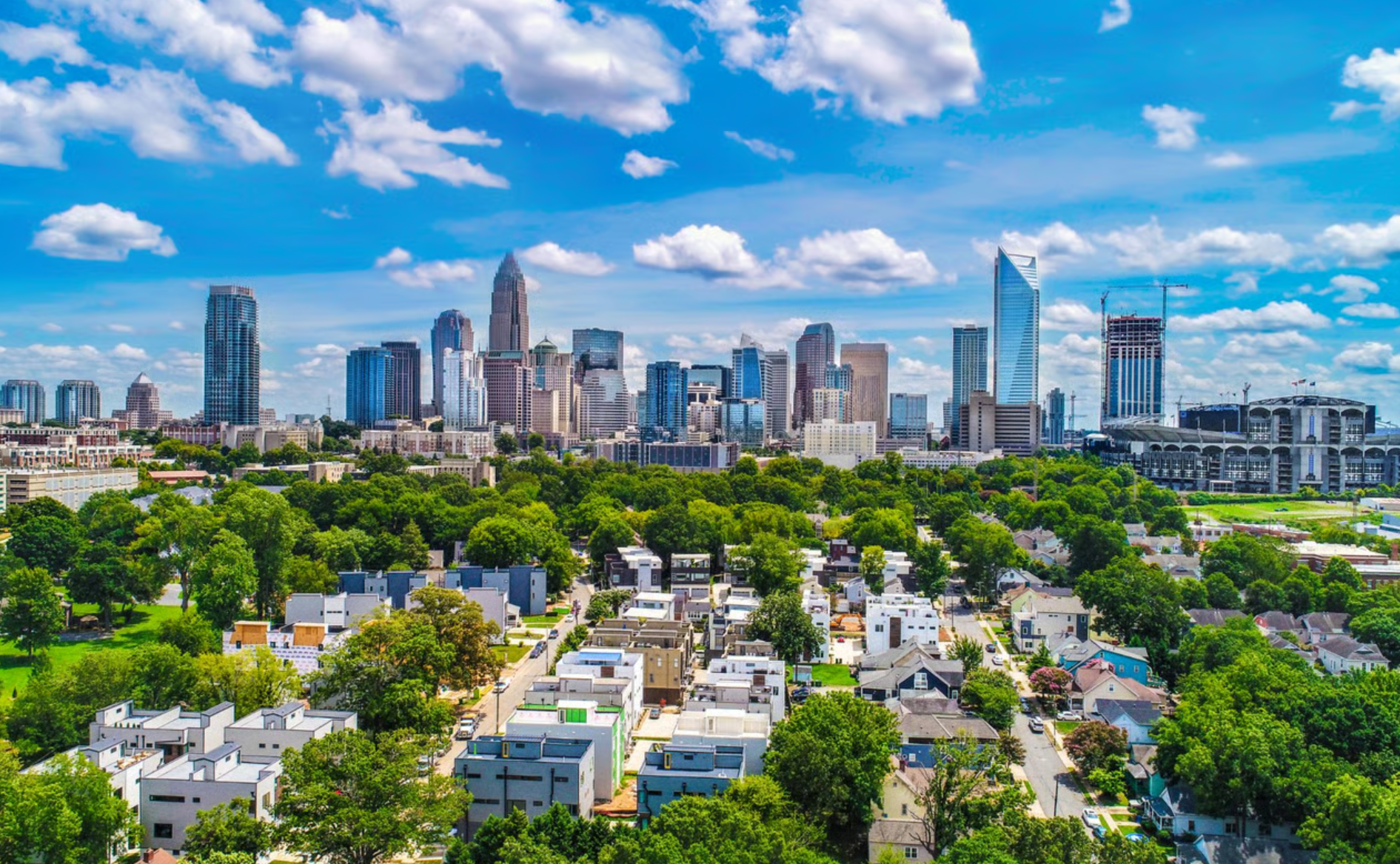 City skyline above green neighborhoods under a bright blue sky with scattered clouds