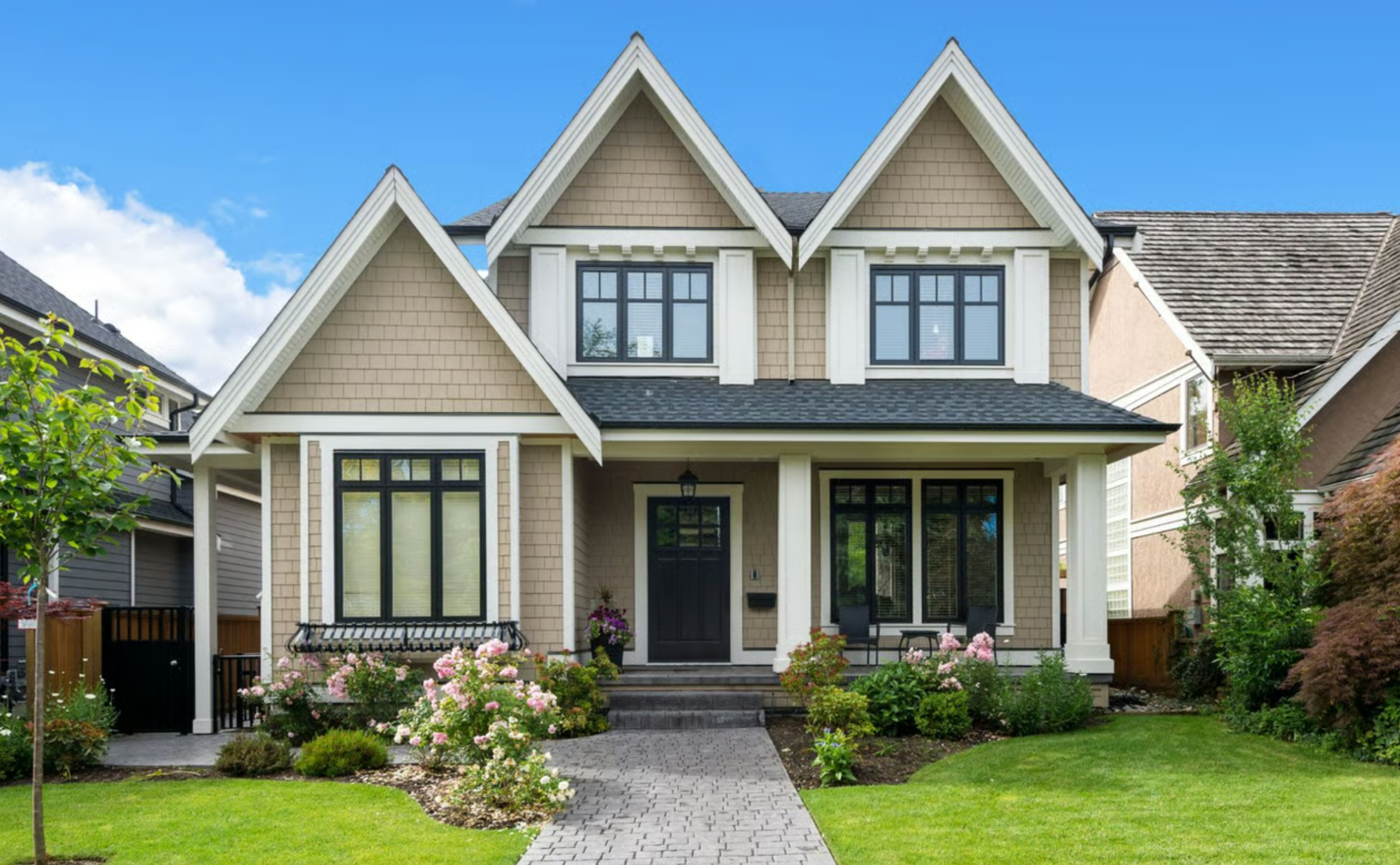 Charming cream-and-gray suburban house with a peaked roof, front porch, and manicured lawn