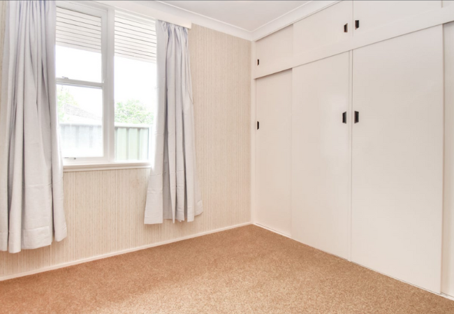 Empty bedroom with tan carpet, beige walls, white built-in closet, and window with curtains.