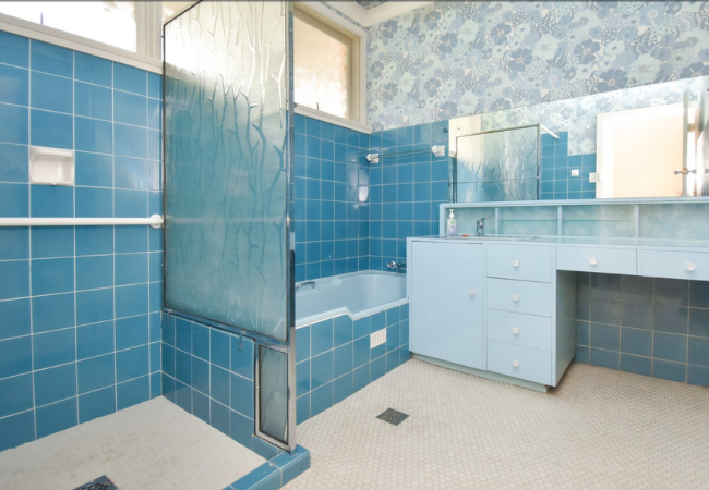 Blue tiled bathroom with shower, tub, and vanity. White floor. Blue floral wallpaper.