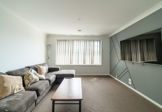 Living room with grey sectional sofa, window with curtains, TV mounted on grey accent wall.
